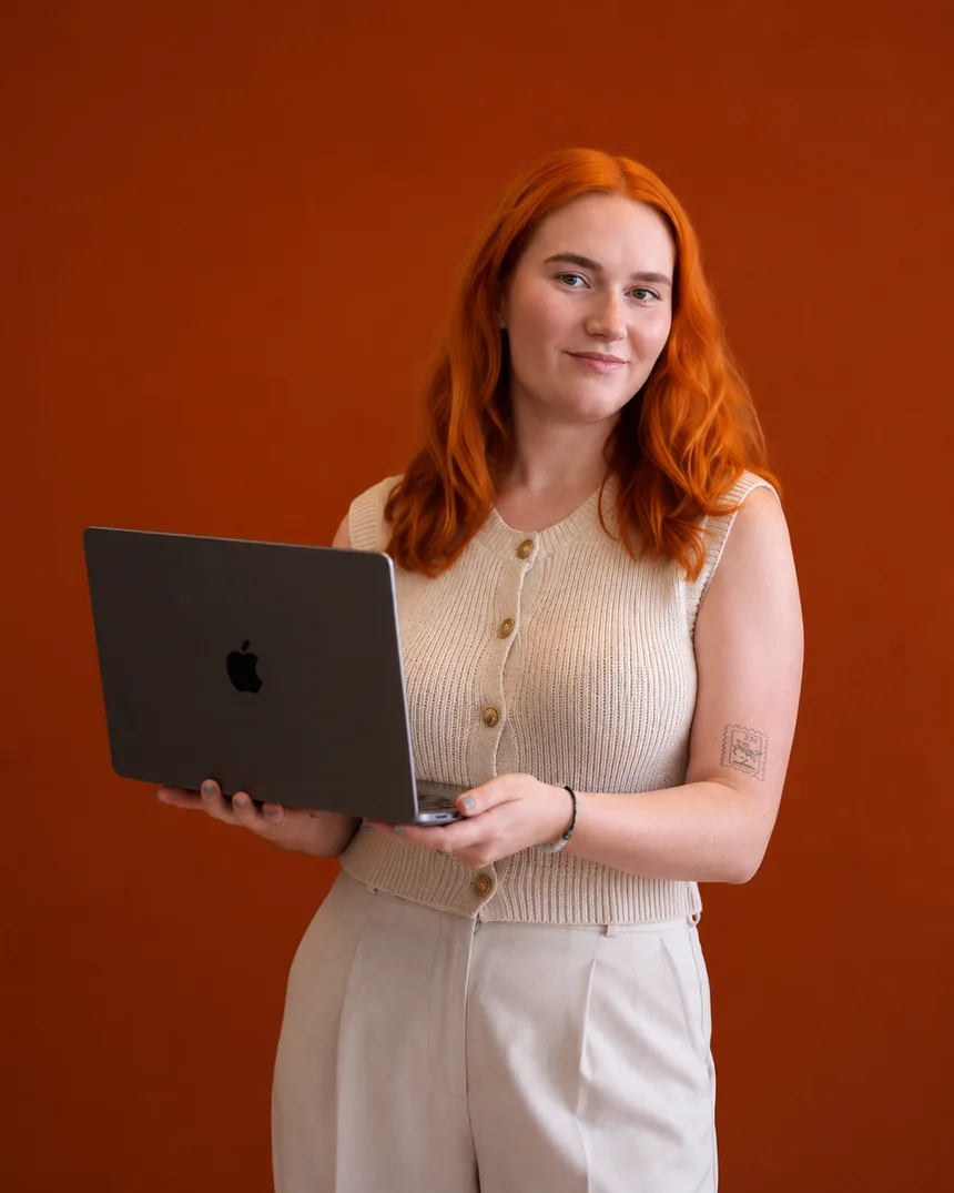 Emi Natividad holding a laptop against a rust-orange wall